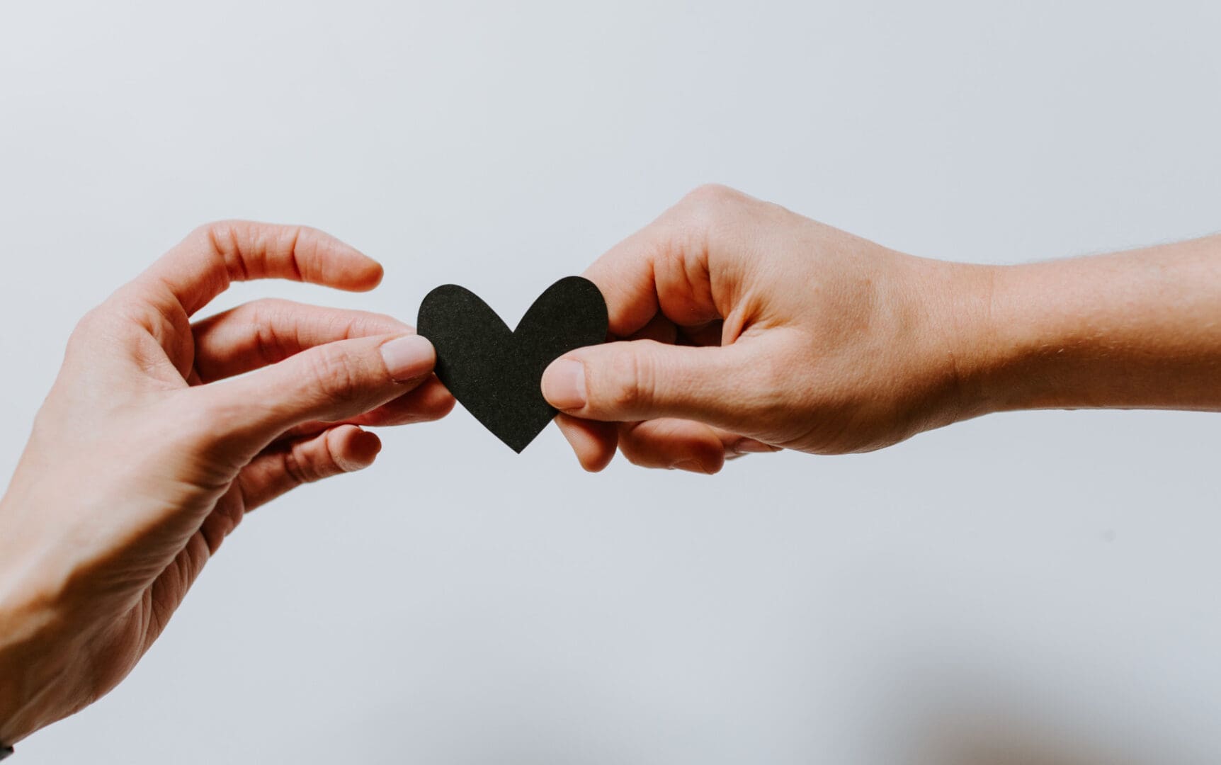 Two people holding a heart shaped piece of paper.